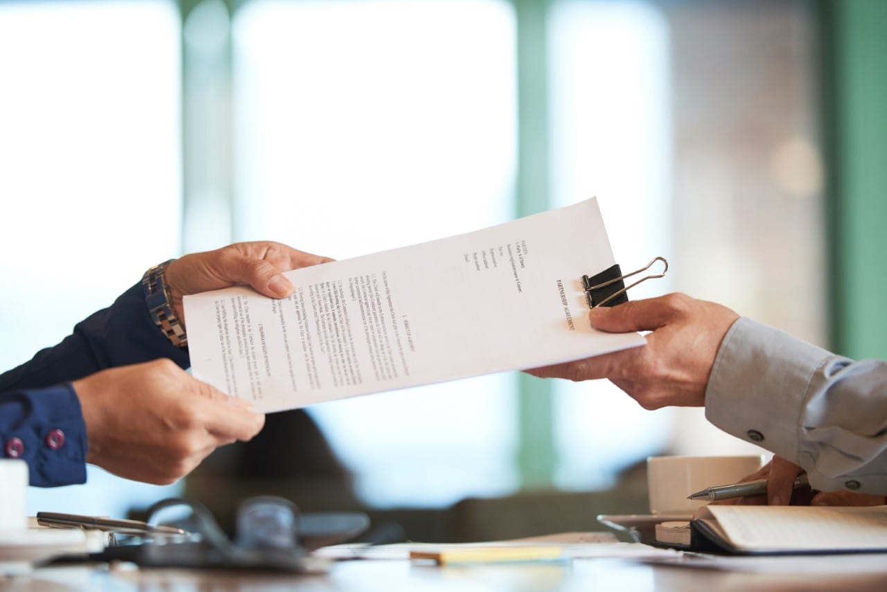 Two people handing over a document across a desk