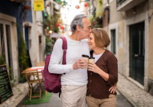 Mature Spouses On Vacation Kissing Clinking Paper Coffee Cups Outdoors
